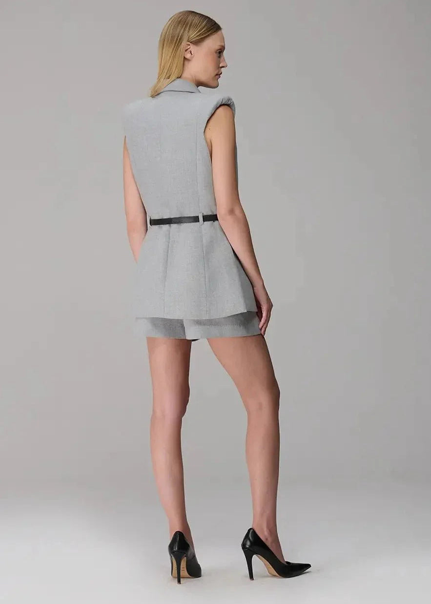 Woman wearing a gray sleeveless dress with cut-out design on a plain background