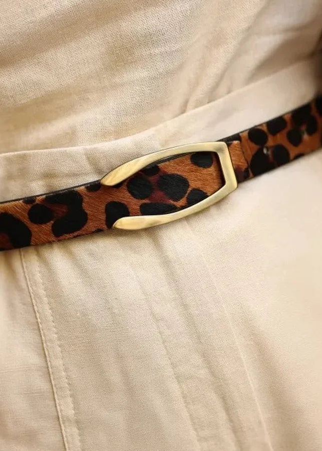 Leopard print belt with a gold buckle worn by a person in beige pants.