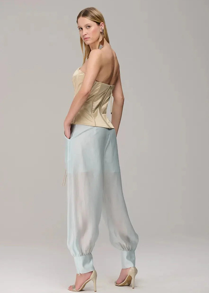 Woman wearing a strapless top and light blue pants on a plain background