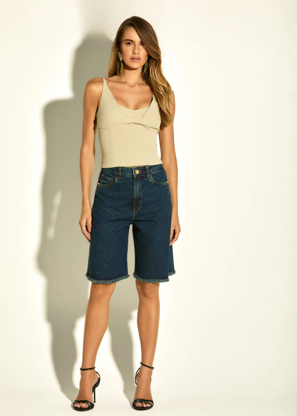 Woman wearing a beige top and blue denim shorts on a white background