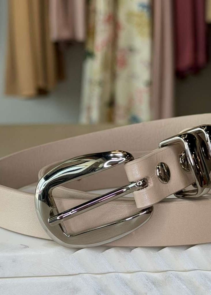 Beige leather belt with a silver buckle on a marble surface.