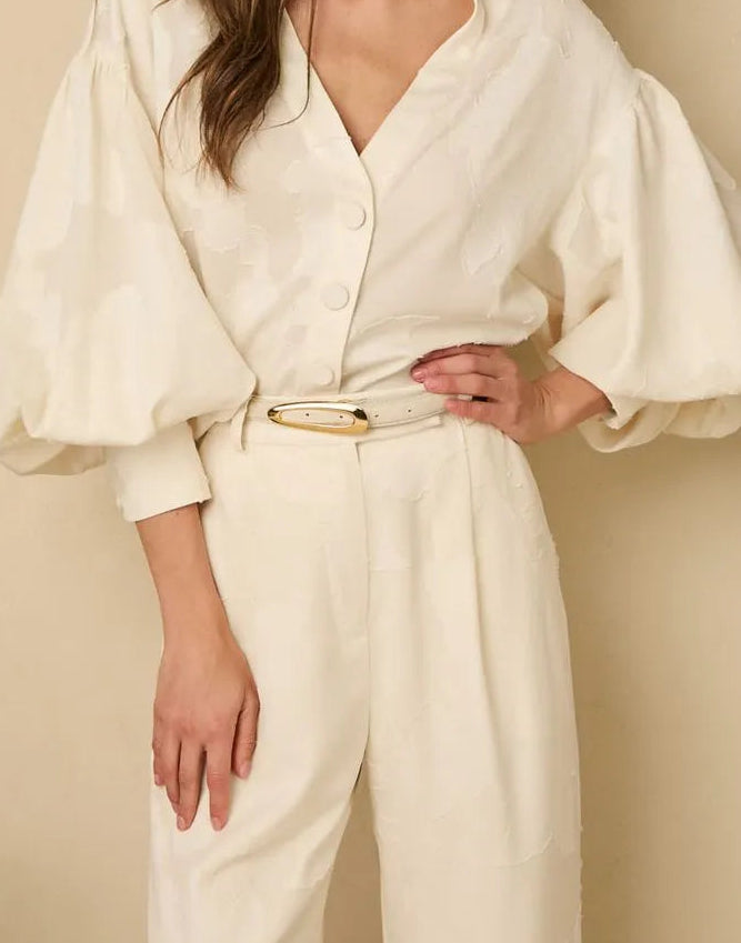 Woman wearing a white outfit with wide sleeves, off white belt against a beige background