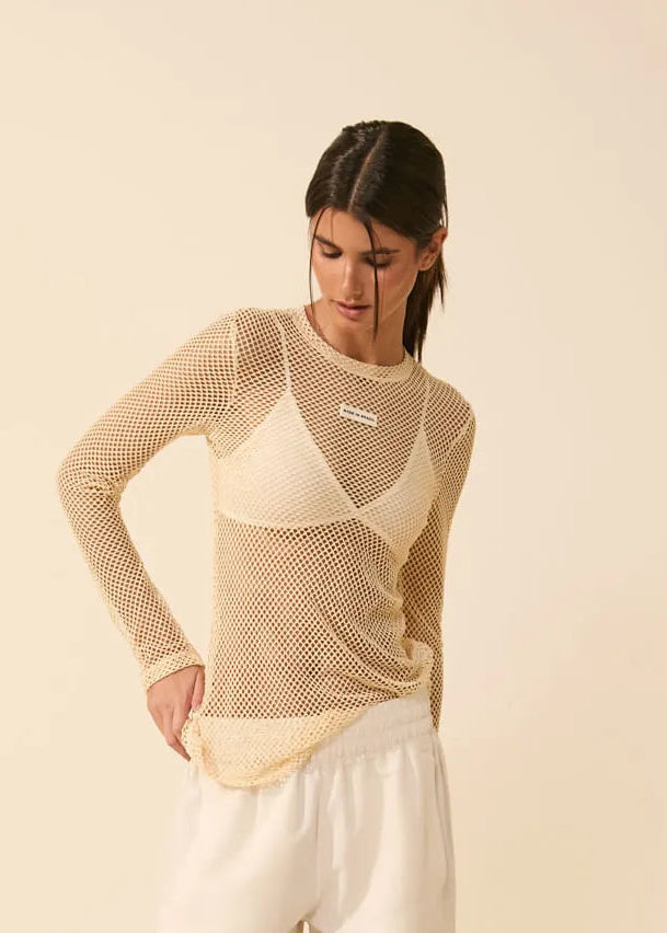 Woman wearing a beige long-sleeve top and white pants against a beige background