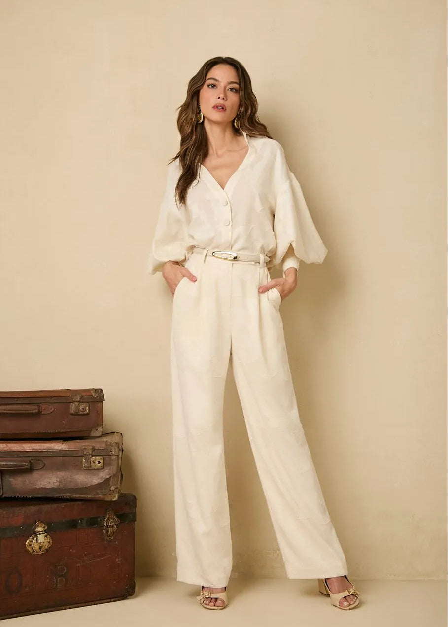 Woman in a white outfit standing next to vintage suitcases against a beige wall.