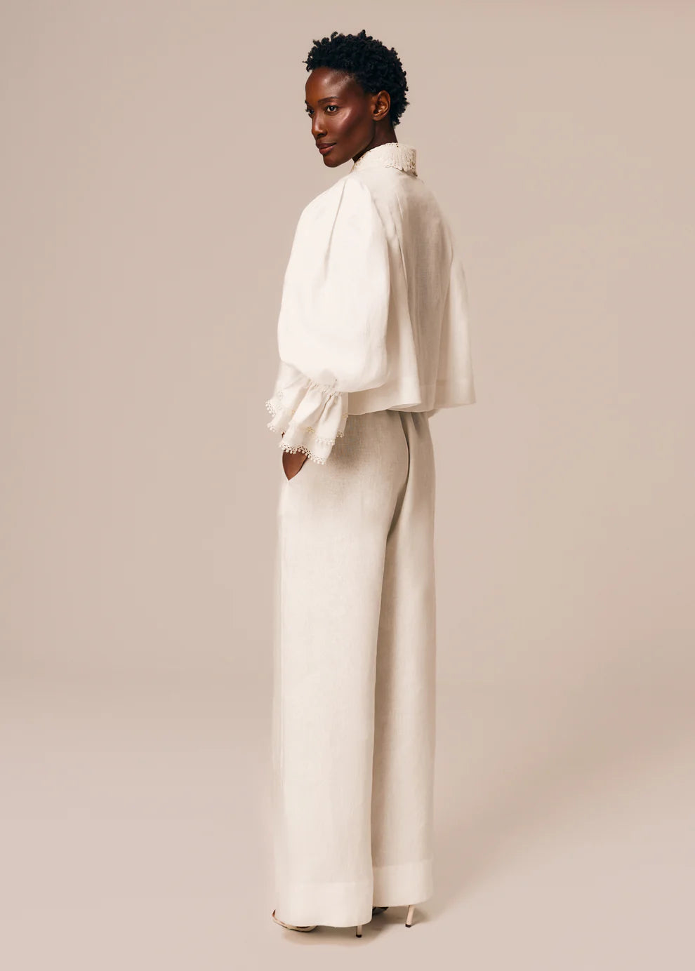 Woman wearing a white outfit with wide-leg pants against a beige background