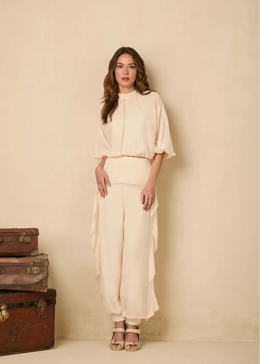 Woman in a cream outfit standing next to vintage suitcases against a beige wall
