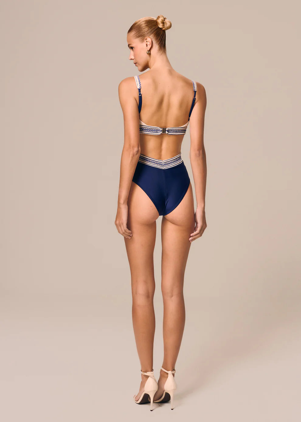 Woman wearing a navy blue swimsuit with white trim on a beige background