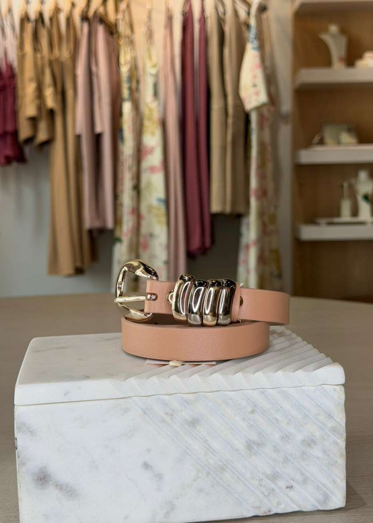 peach belt with gold and silver buckles on a marble box in a clothing store setting