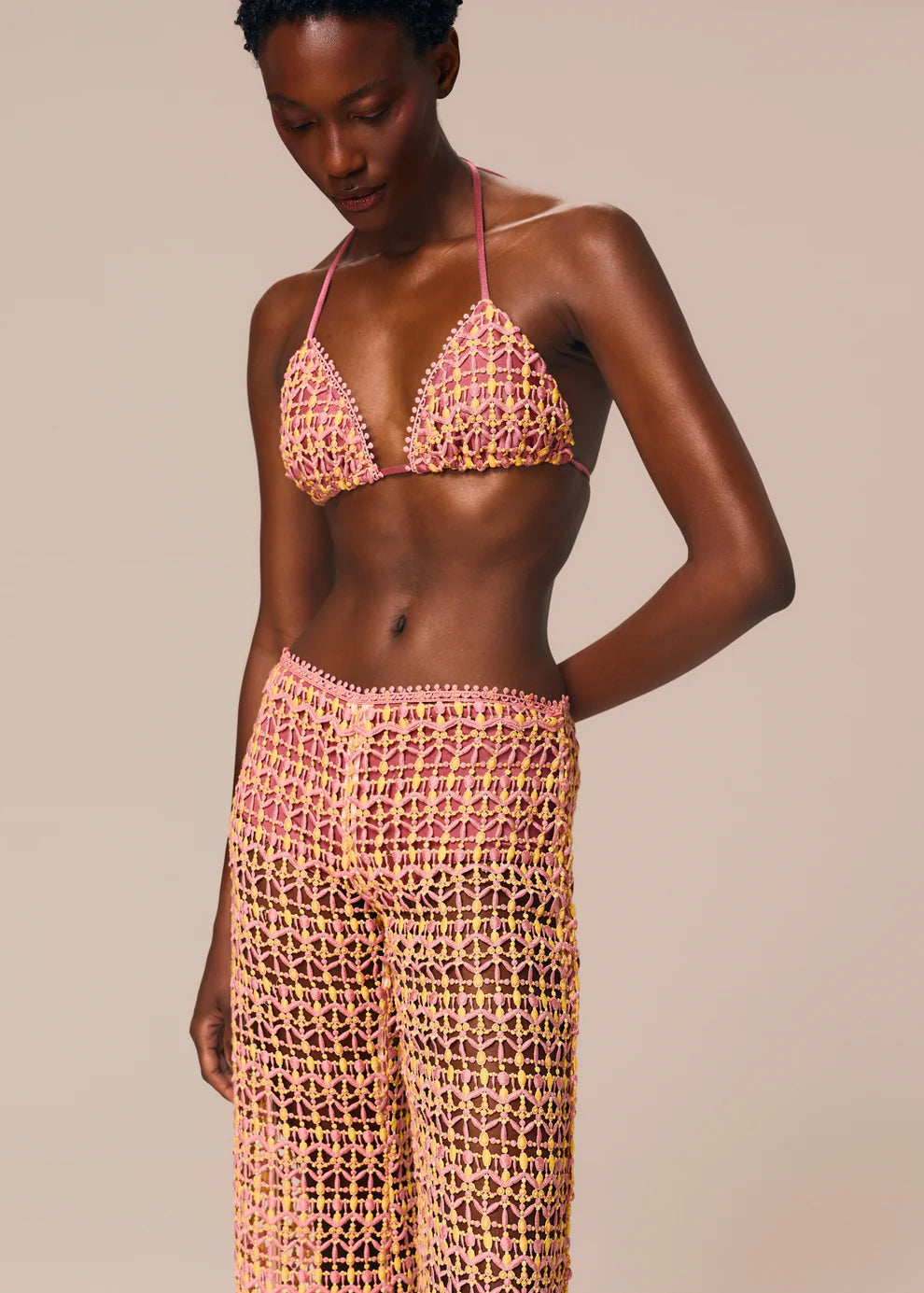 Woman wearing a pink crochet bikini set against a beige background