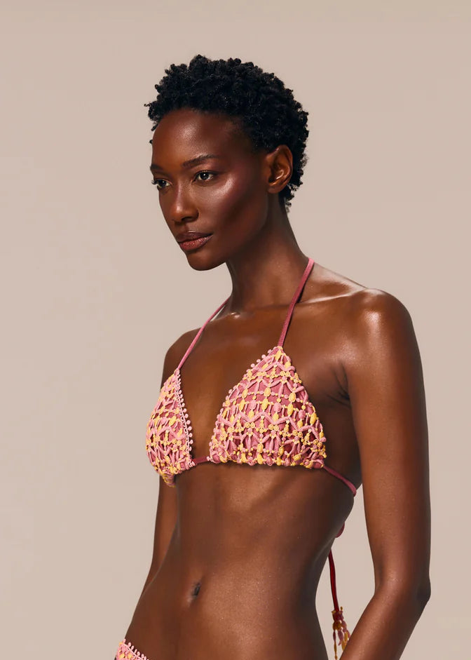 Woman wearing a pink crochet bikini against a beige background