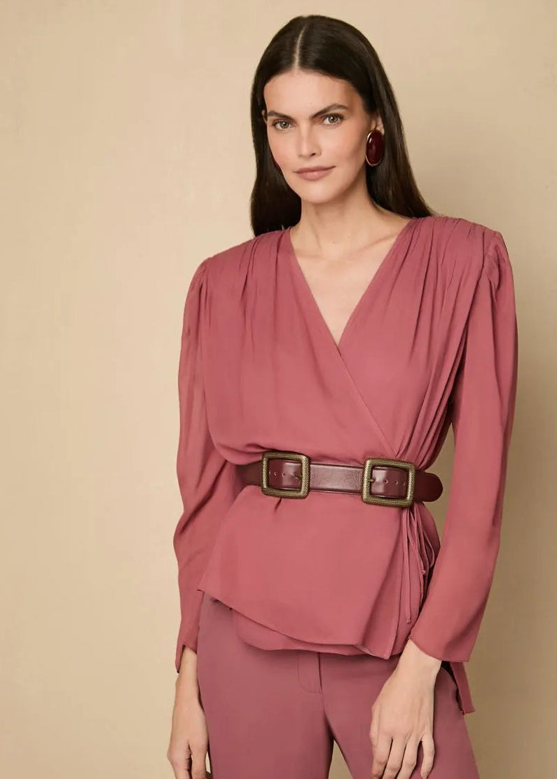 Woman wearing a pink outfit with a belt against a beige background