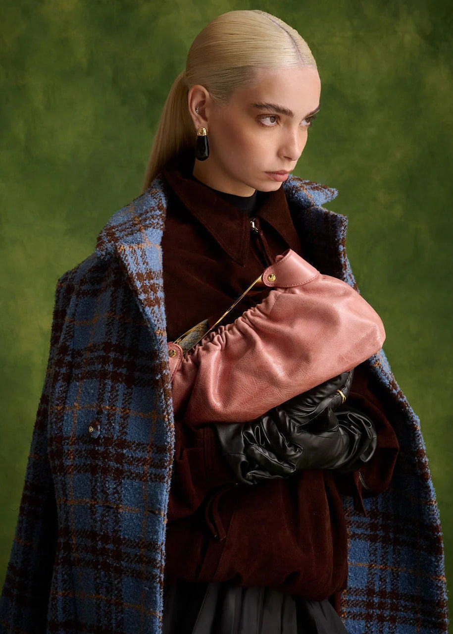 Person wearing a blue and brown plaid coat with a pink bag against a green background