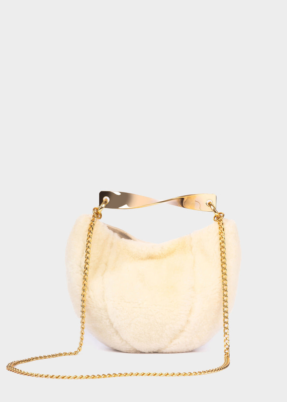 A cream-colored crescent handbag with a gold-tone metal handle and a gold chain shoulder strap, set against a solid light gray background.