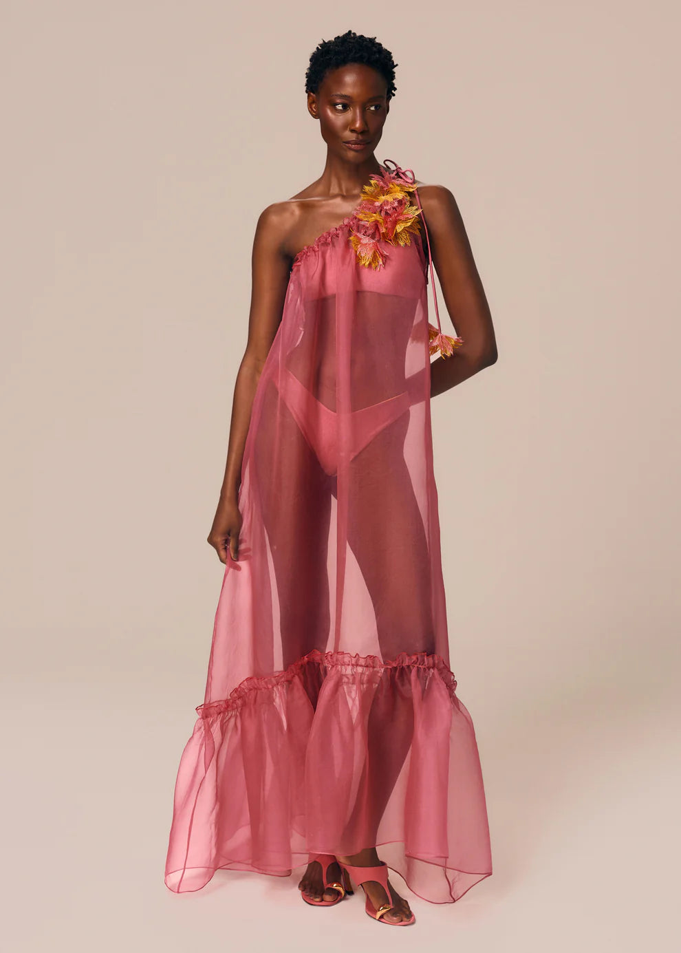 Woman wearing a pink sheer dress with floral accents against a beige background