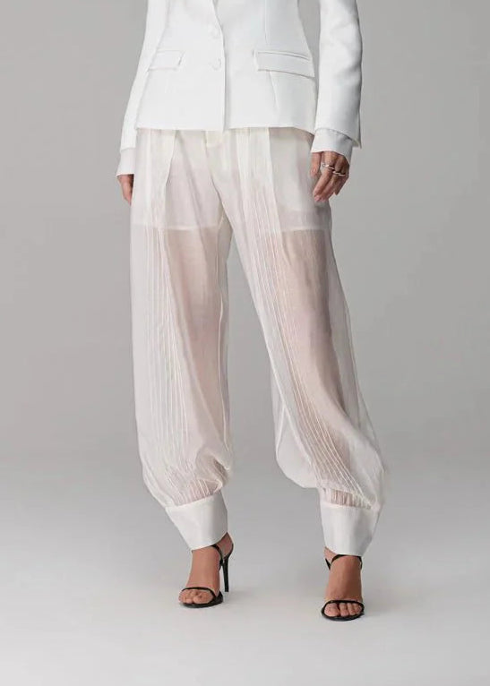 Woman wearing a white suit with sheer pants on a gray background