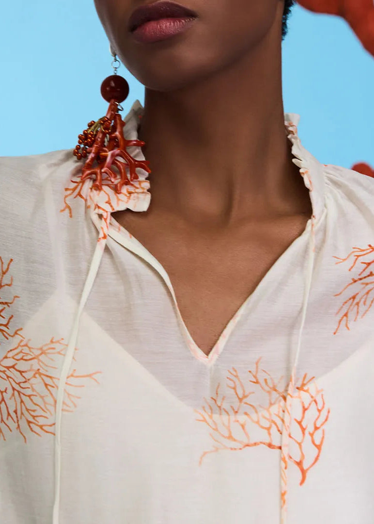 Woman wearing a white blouse with orange coral patterns against a blue background