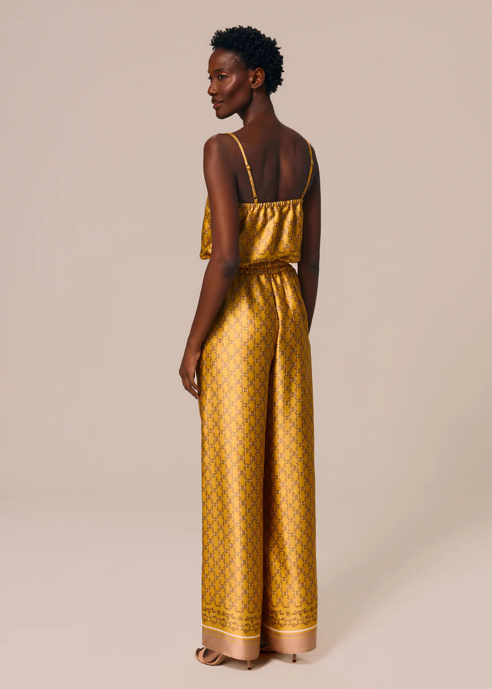 Woman wearing a gold patterned pants against a beige background