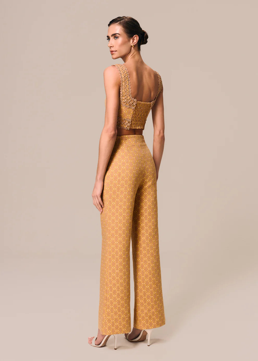 Woman wearing a mustard yellow patterned outfit on a beige background